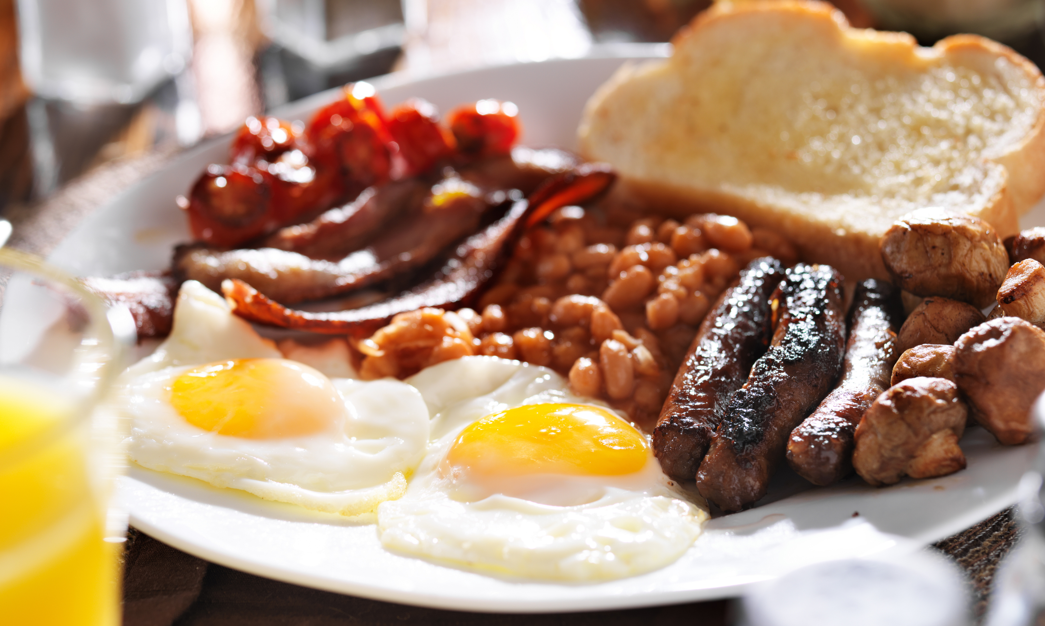 Image of a full English breakfast with bacon, eggs, sausages, toast, mushrooms, beans and tomatoes.