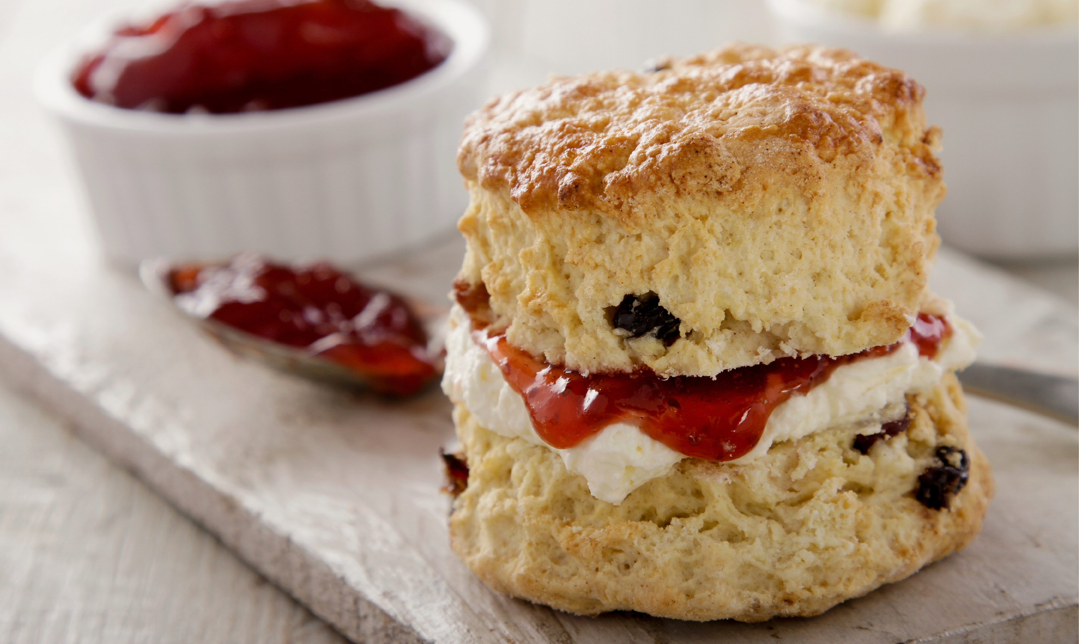 Image of a scone with cream and jam inside. a pot of jam on the side.